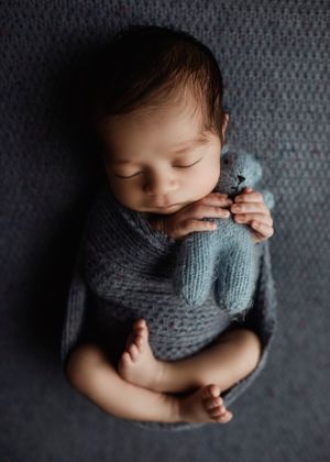 Peaceful sleeping newborn in gray knit wrap on textured background.