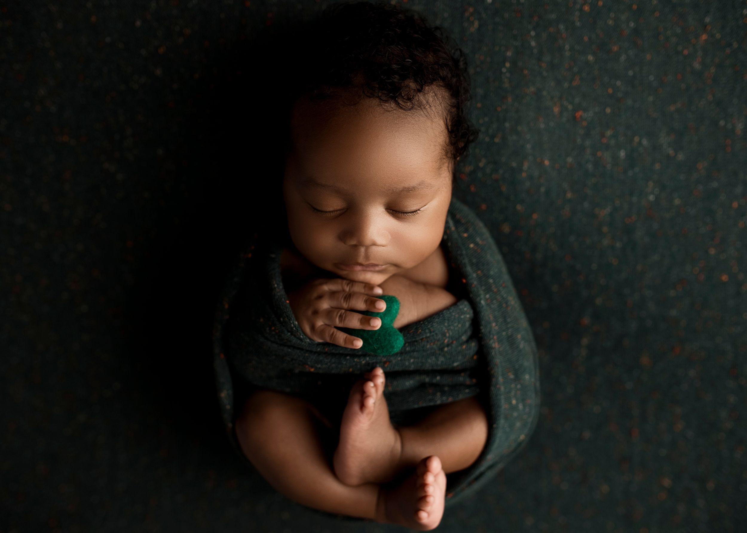 Sleeping newborn wrapped in teal blanket during professional photo session.