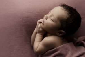 Sleeping baby in peaceful repose against pink background.