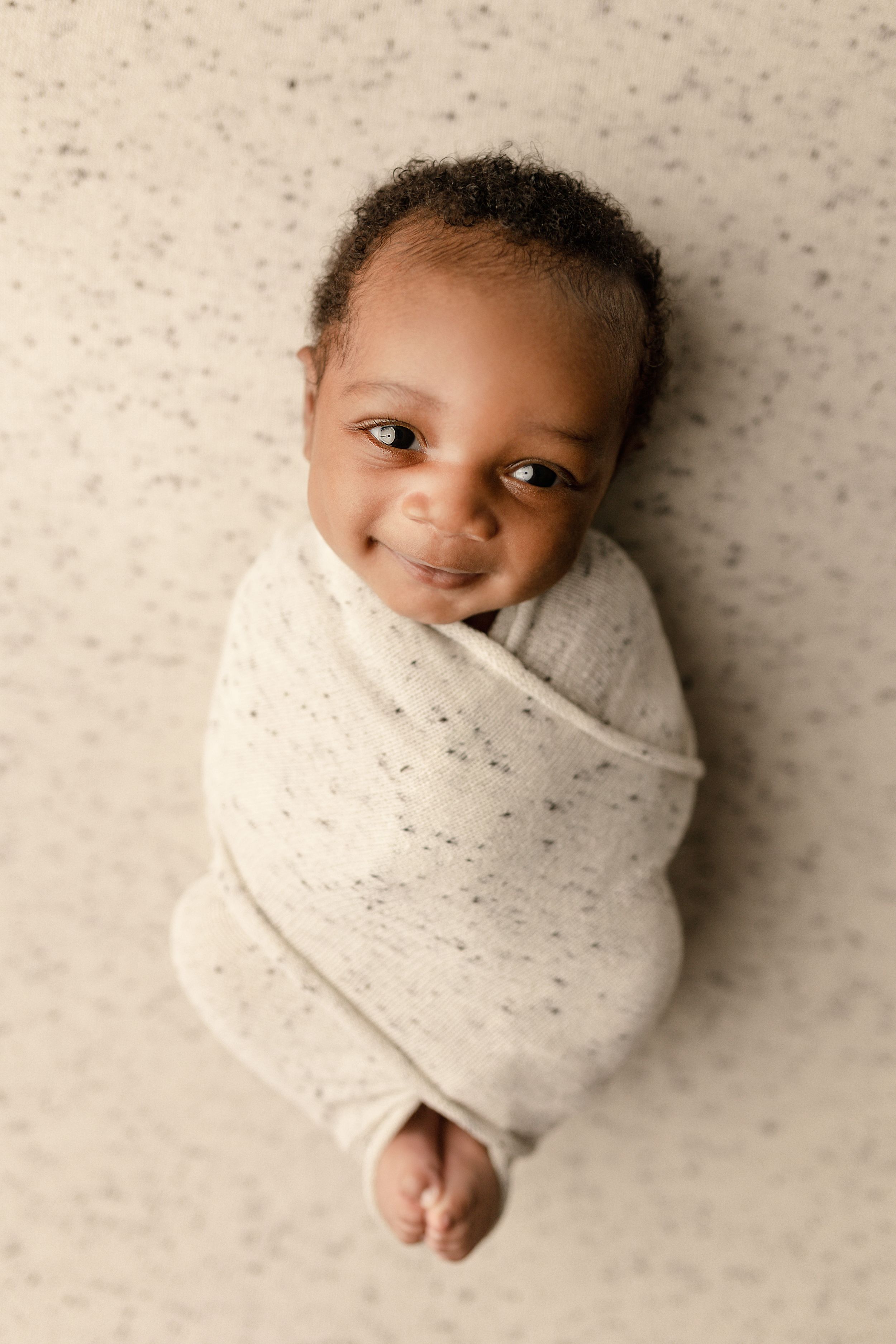Overhead portrait of infant swaddled in speckled beige wrap.