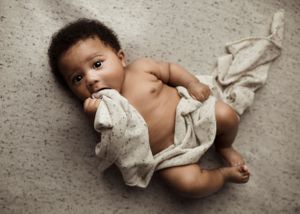 Baby lying on gray carpet wearing light colored fabric wrap.