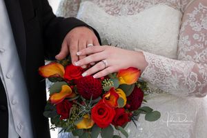 Detail shots of colorful wedding bouquet with red and orange flowers against lace dress.