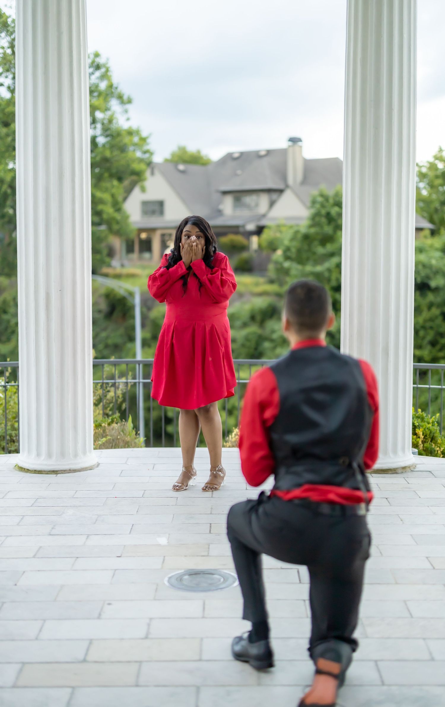 A person in a red dress poses between classical white columns during a photo session.