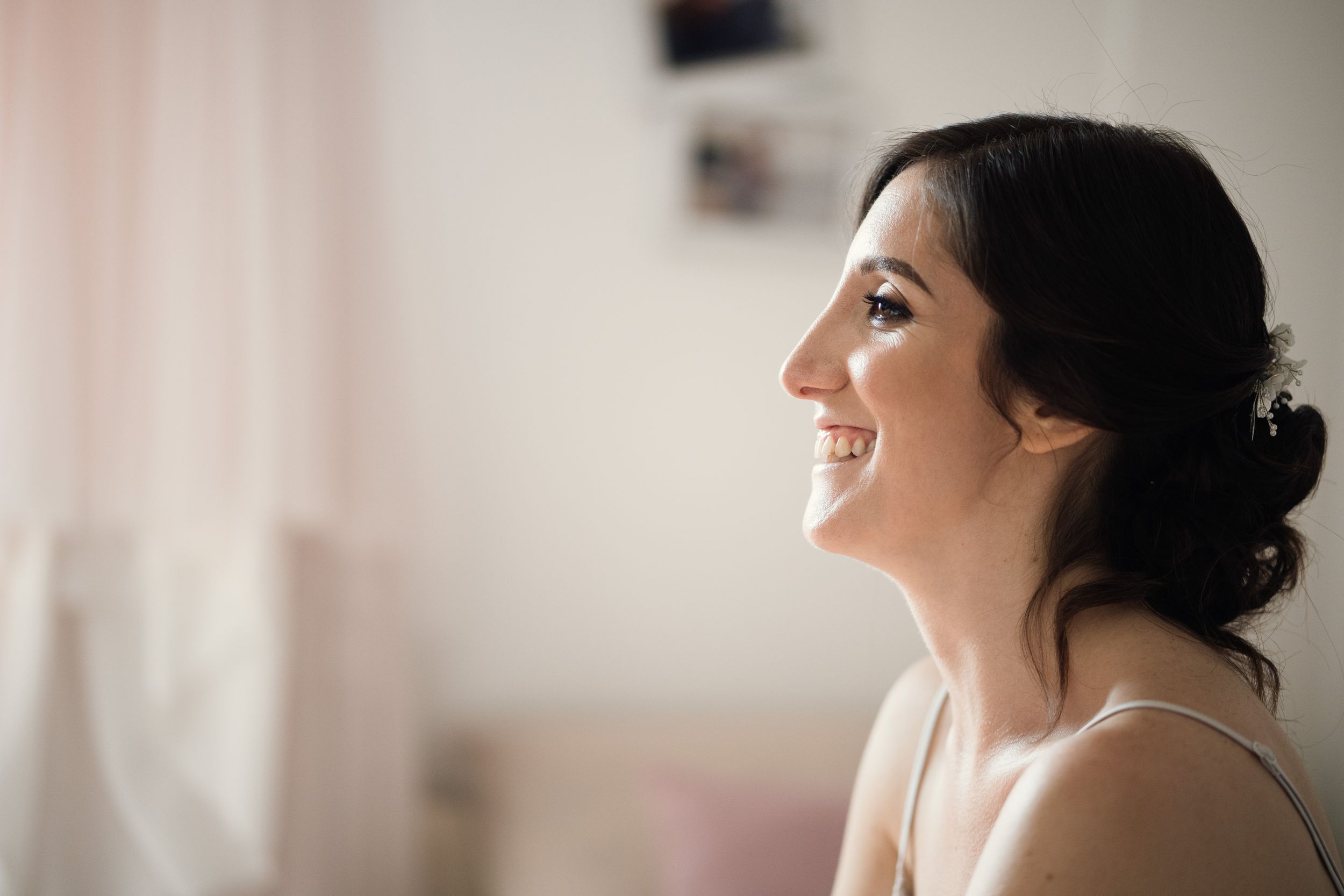Profile view of someone in a light-colored top with dark upswept hair smiling and looking upward.