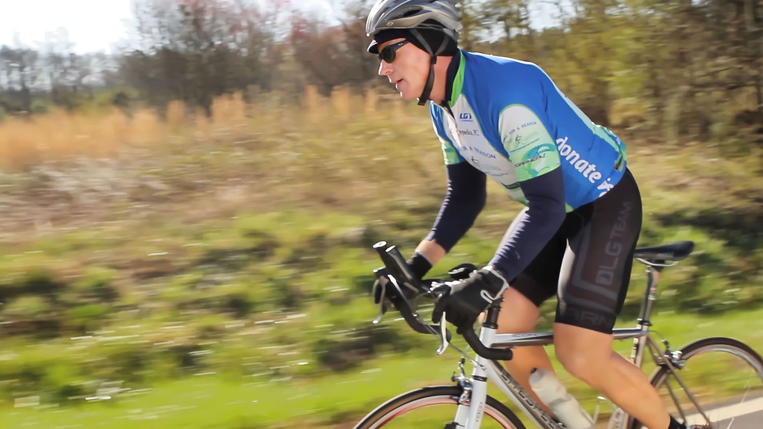Cyclist in blue jersey riding a road bike through autumn countryside scenery.