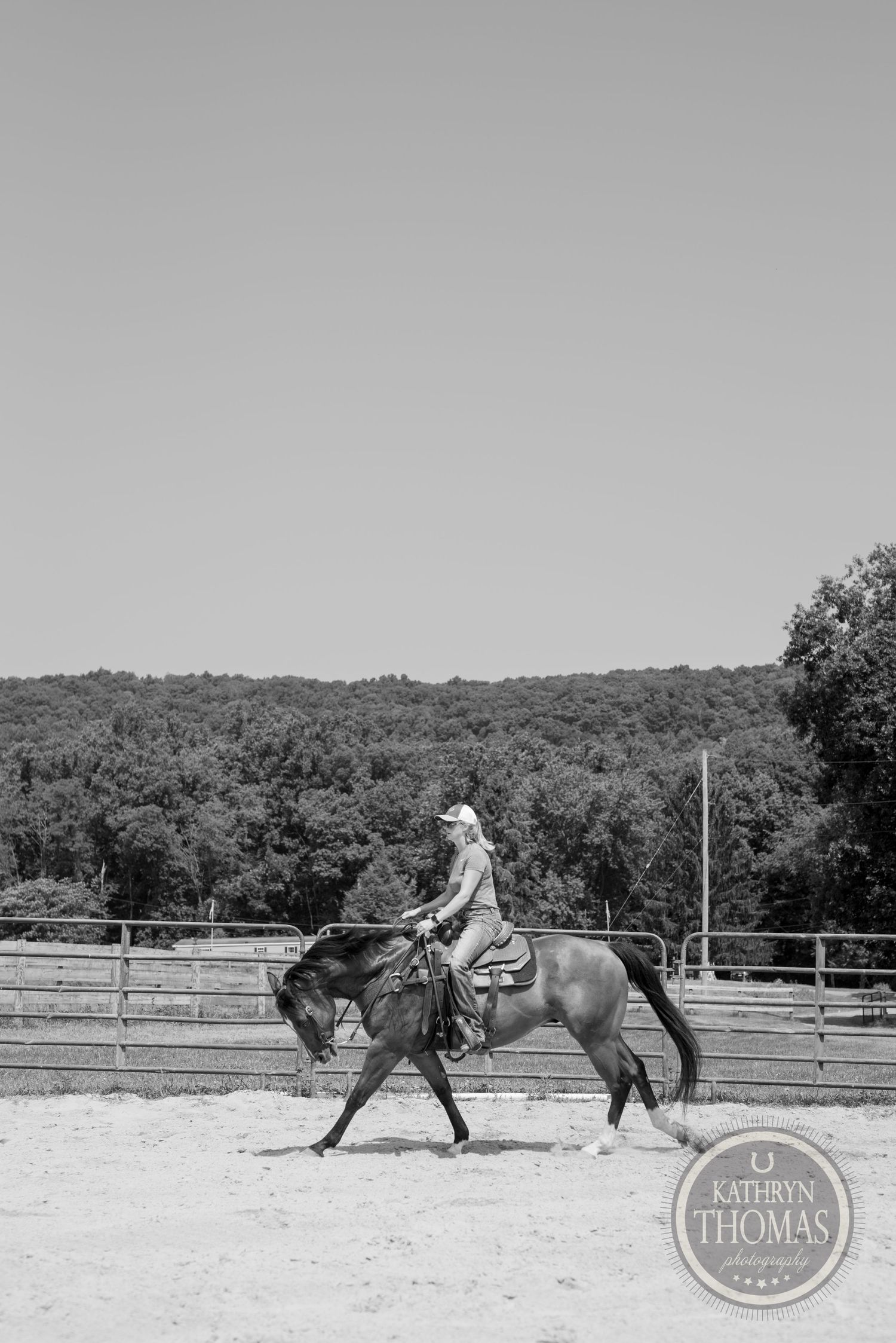 Black and white image of horse and rider practicing in arena with mountainous backdrop.