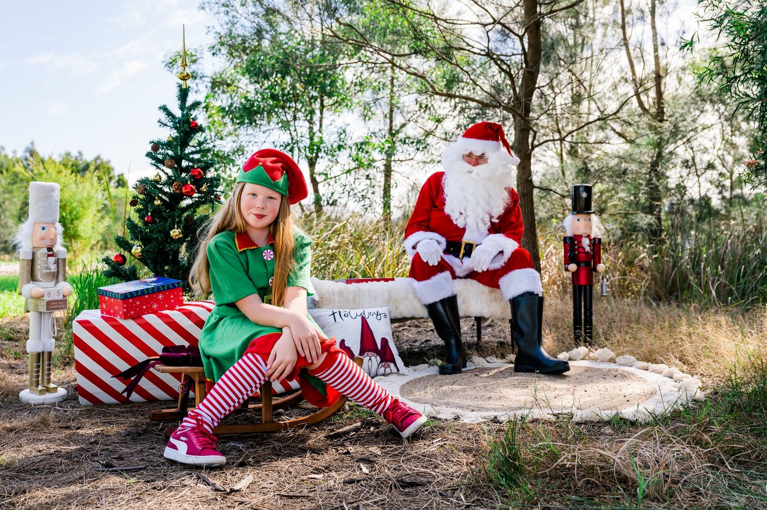 Christmas scene with decorated tree, wrapped presents, and holiday characters in outdoor setting.