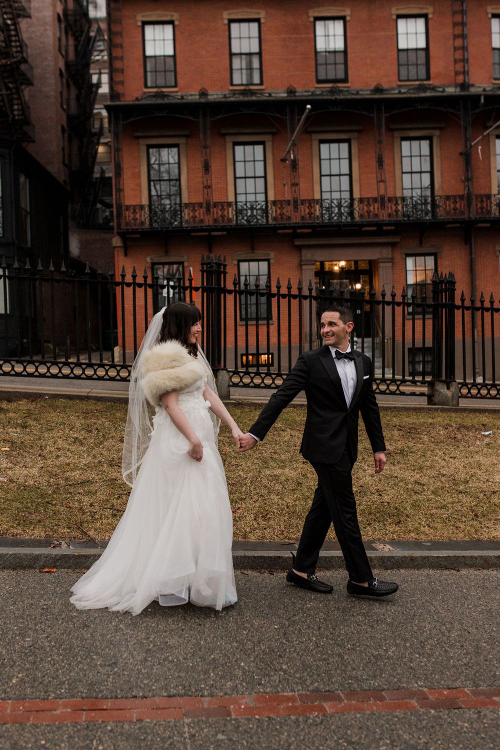 A couple dressed in wedding attire walks hand-in-hand through Boston Common.