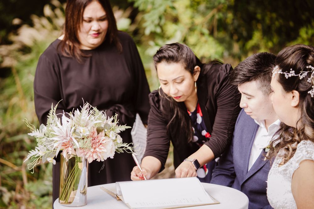 Wedding party gathered around a table signing documents during an outdoor ceremony.