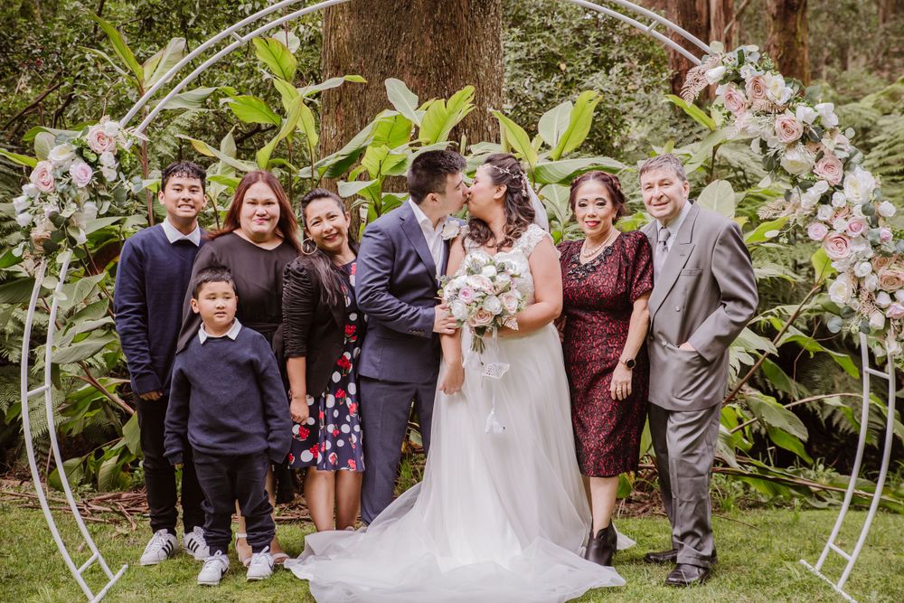 Wedding party poses together under a circular floral arch in a garden setting.