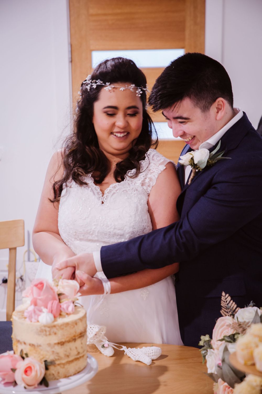 Newlyweds cut their naked wedding cake decorated with pink roses.