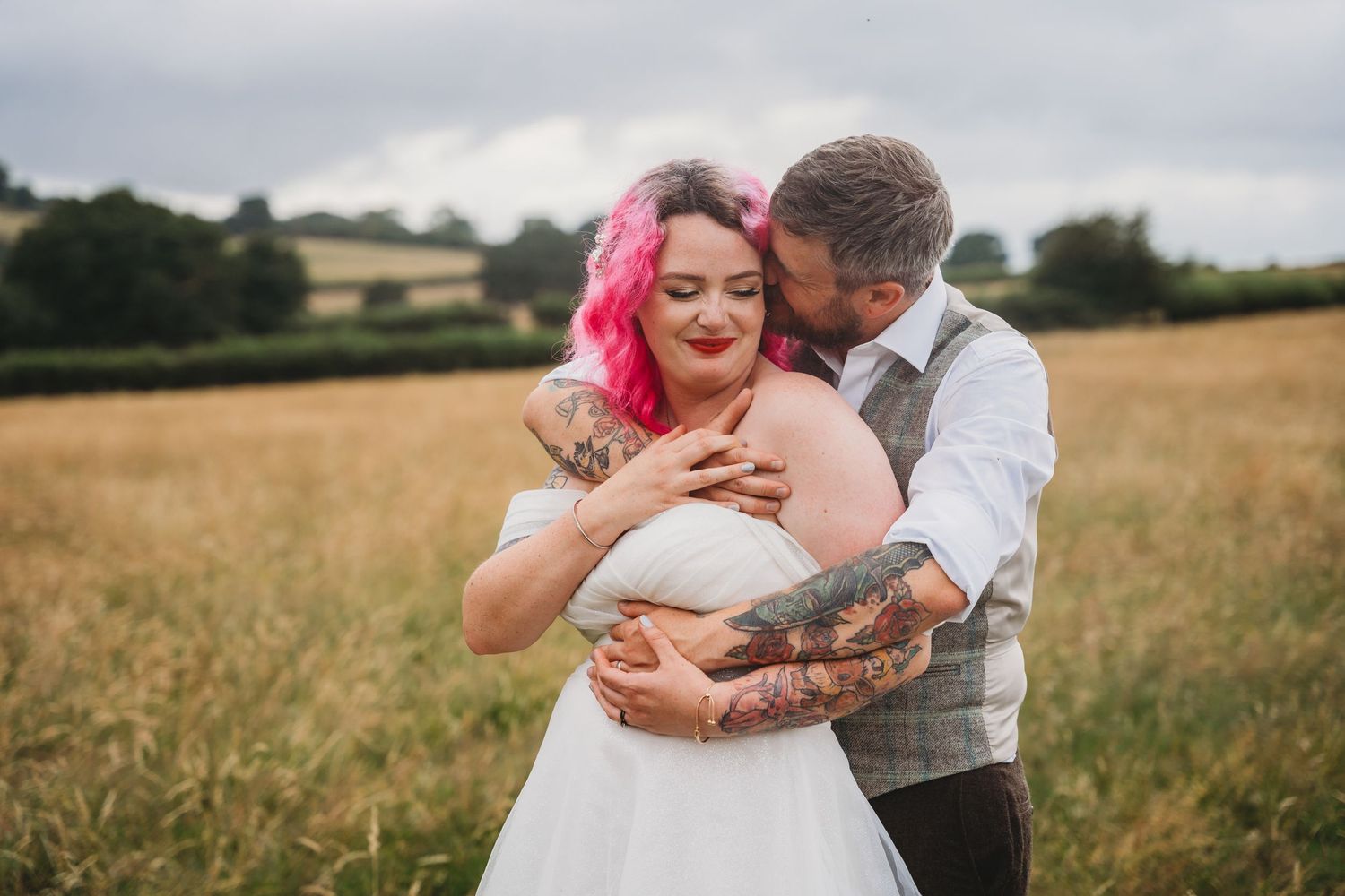 Romantic couple embrace in sunny field during wedding photoshoot.