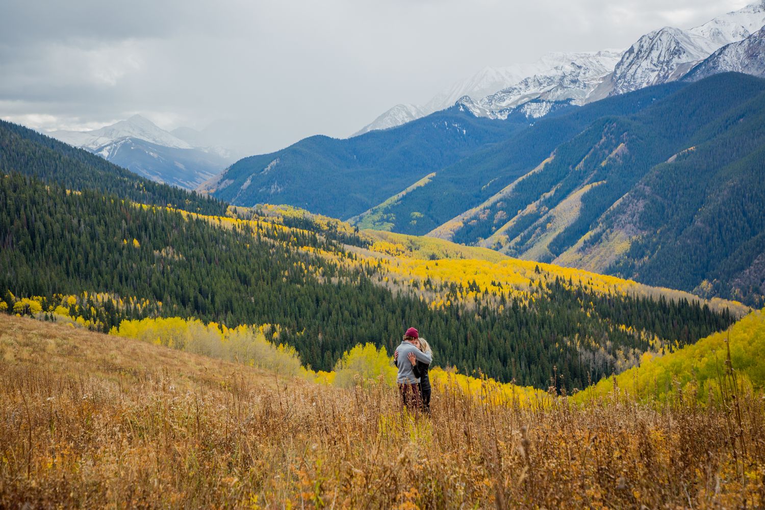 A scenic mountain landscape with golden autumn foliage and snow-capped peaks in the distance.