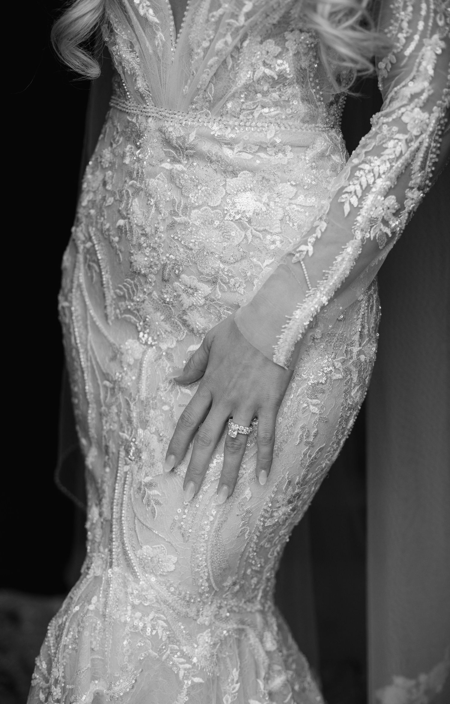Close-up detail of intricate lace wedding dress and engagement ring.