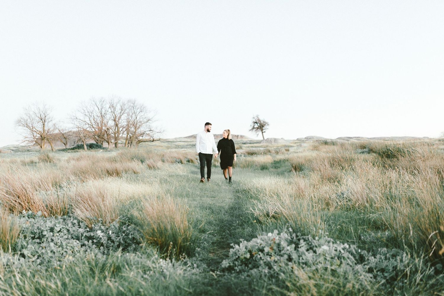 Two silhouetted figures walking together through tall grass on a hillside.