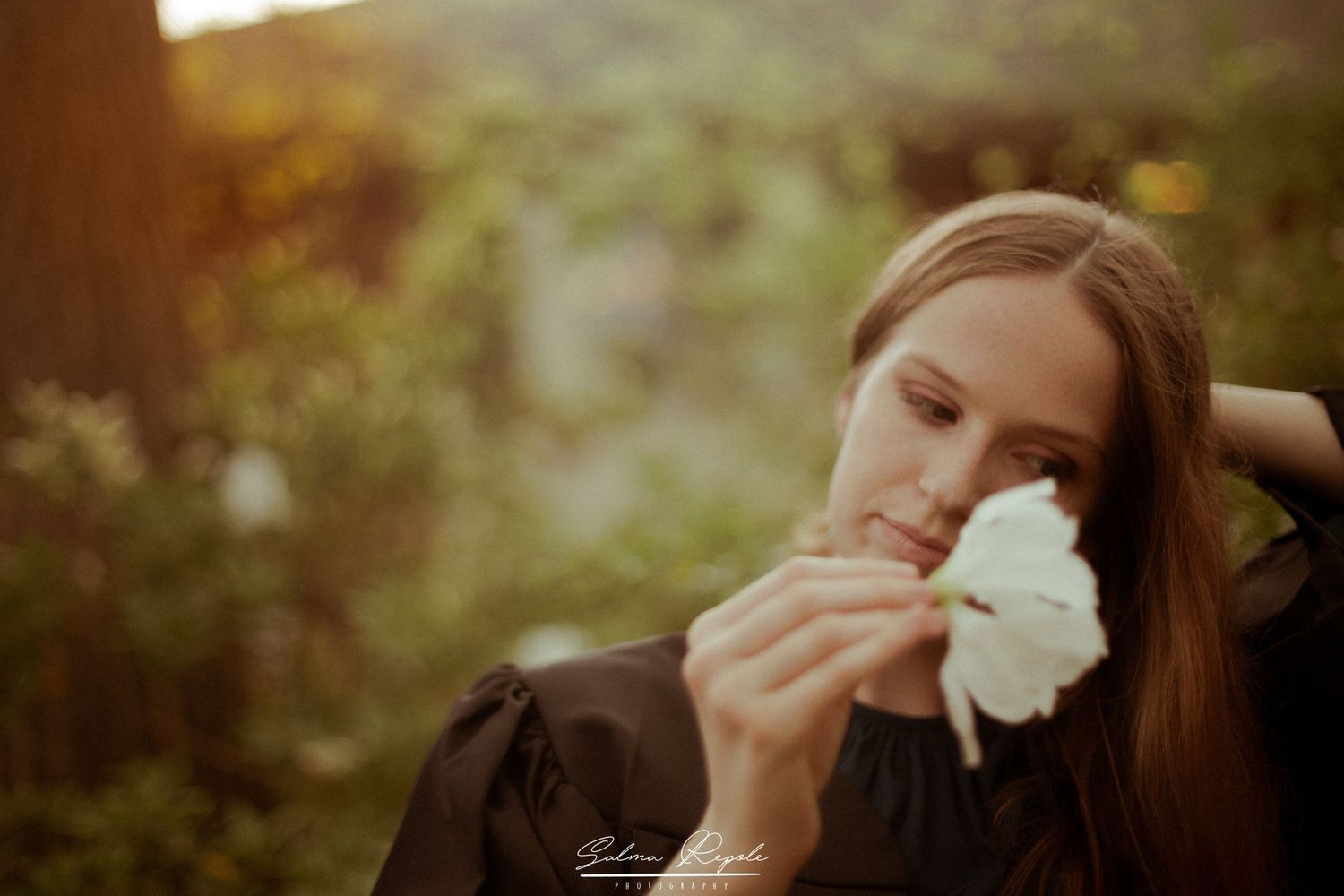 Person holding a white flower while laughing during a natural light portrait session.
