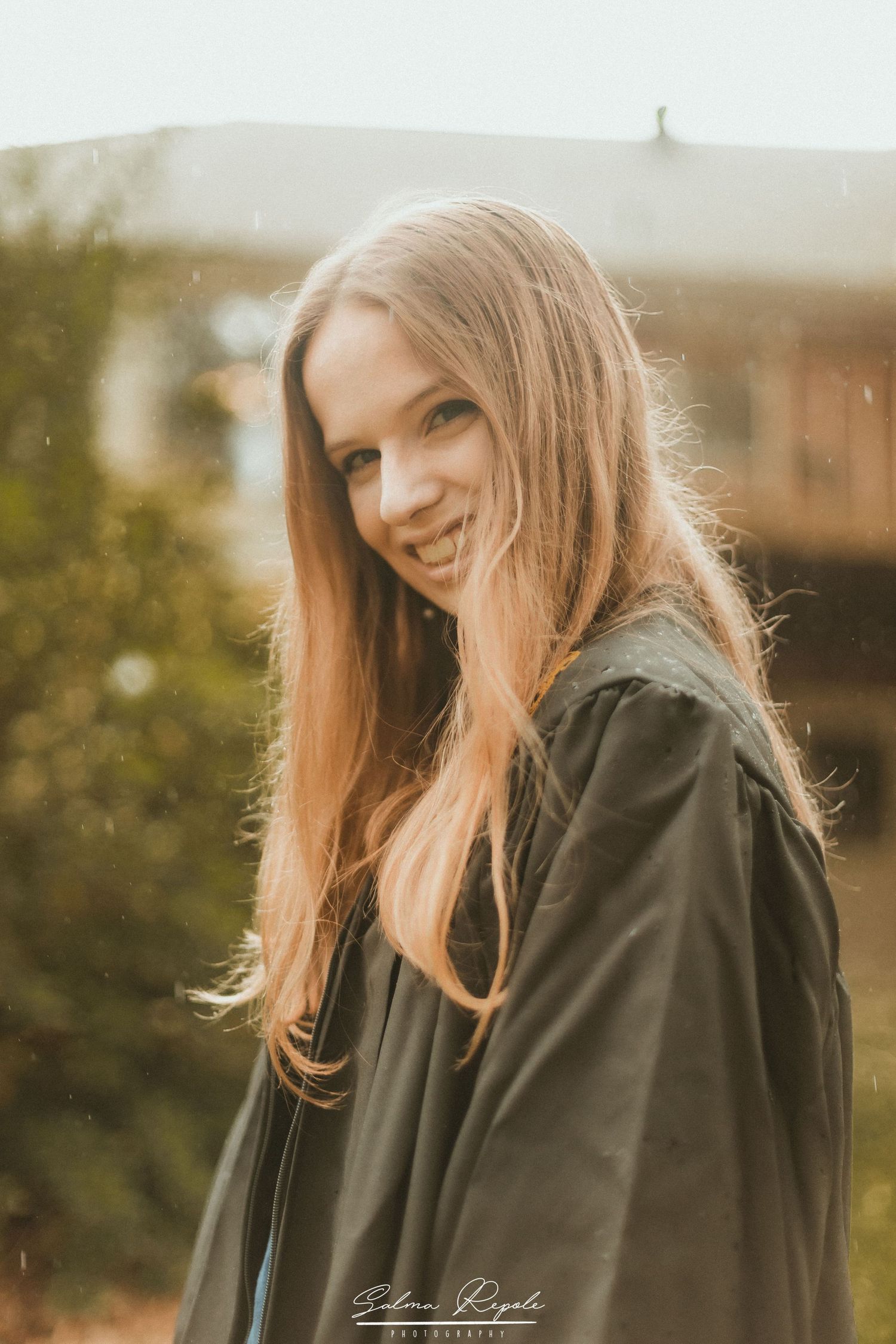 Warm sunlit portrait of someone in a dark jacket smiling during a golden hour photoshoot.