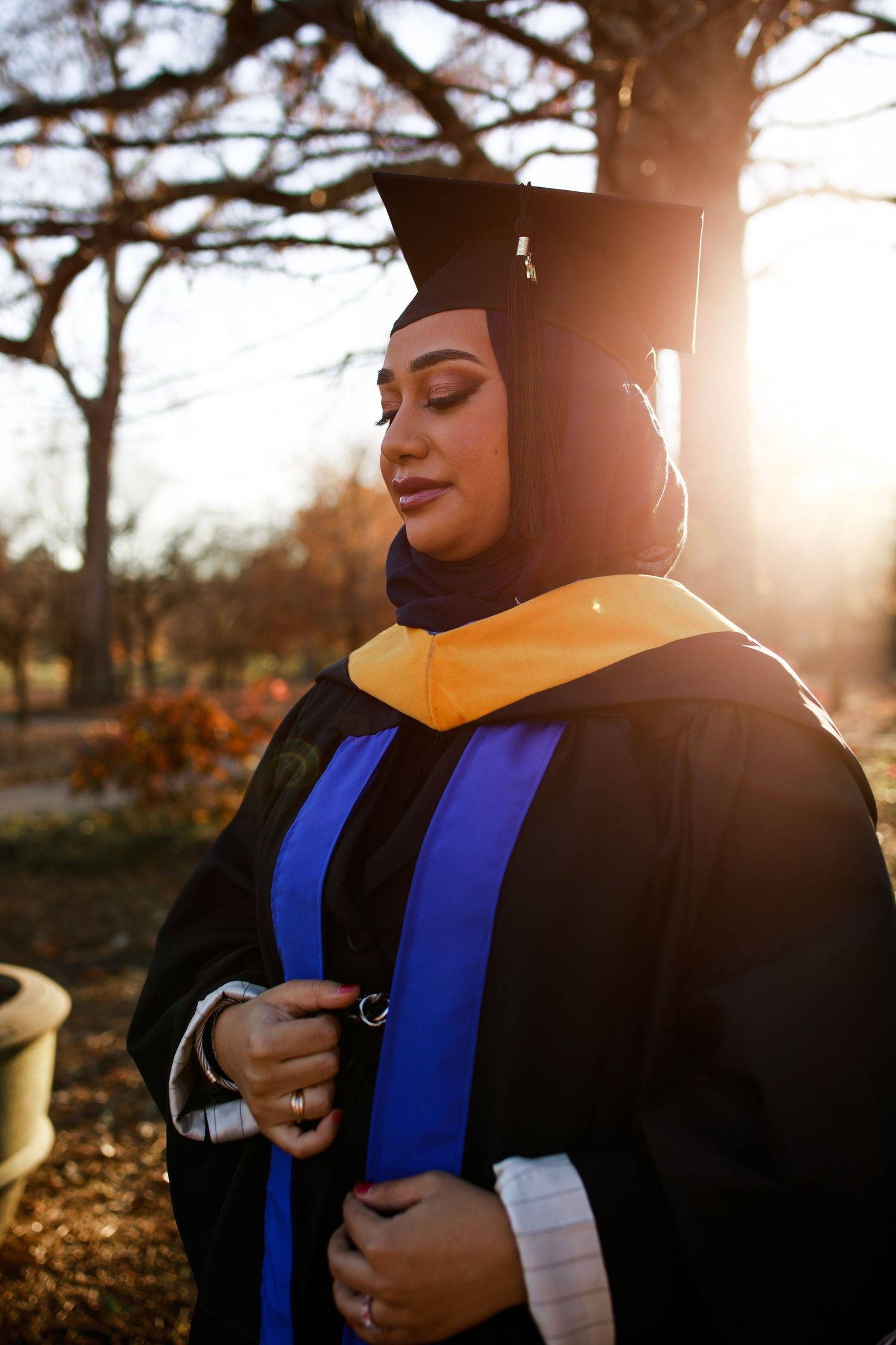 Graduate in academic regalia stands in golden sunlight during sunset ceremony.
