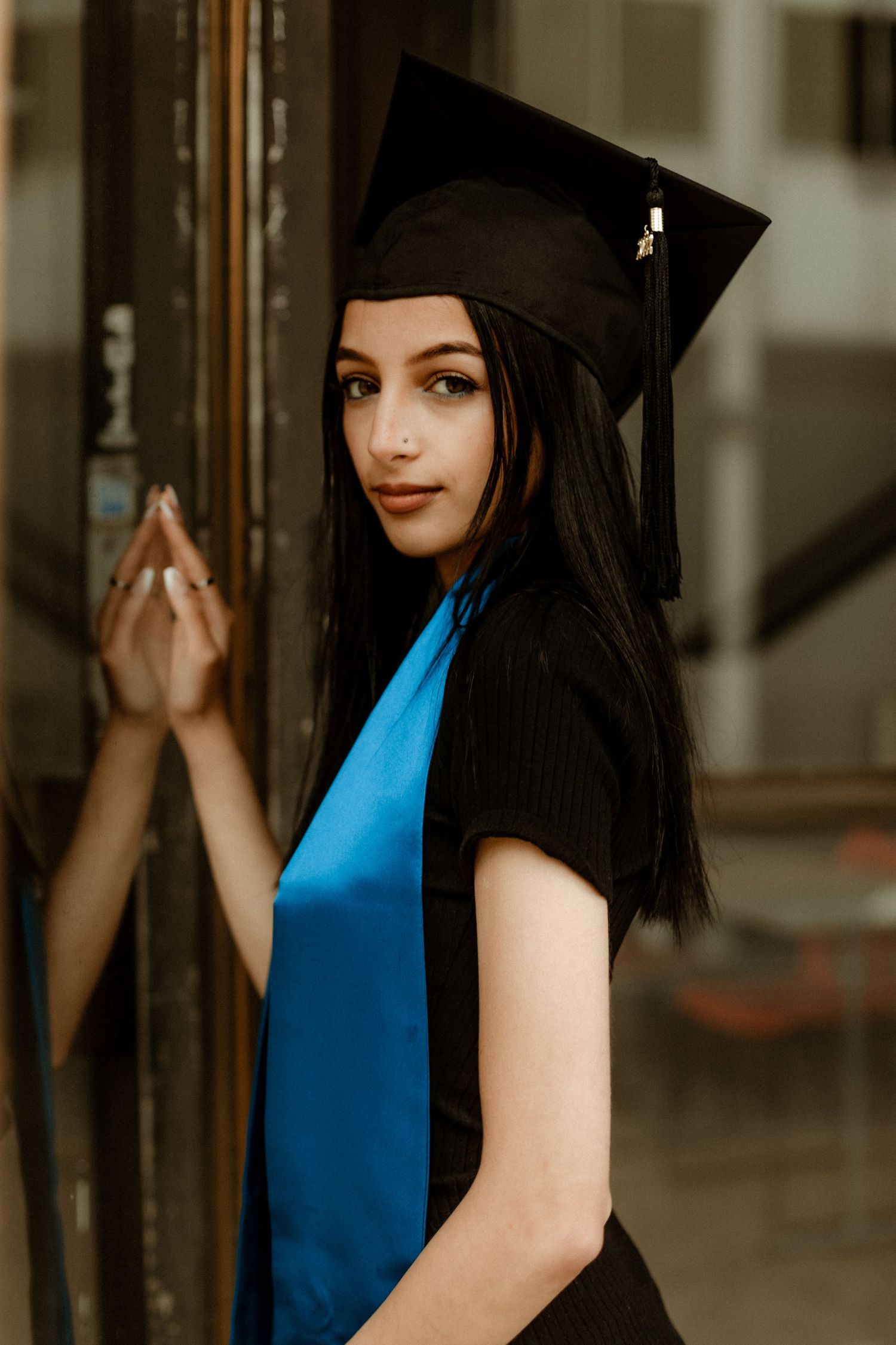 A graduate in cap and gown with blue stole poses against a wooden door.