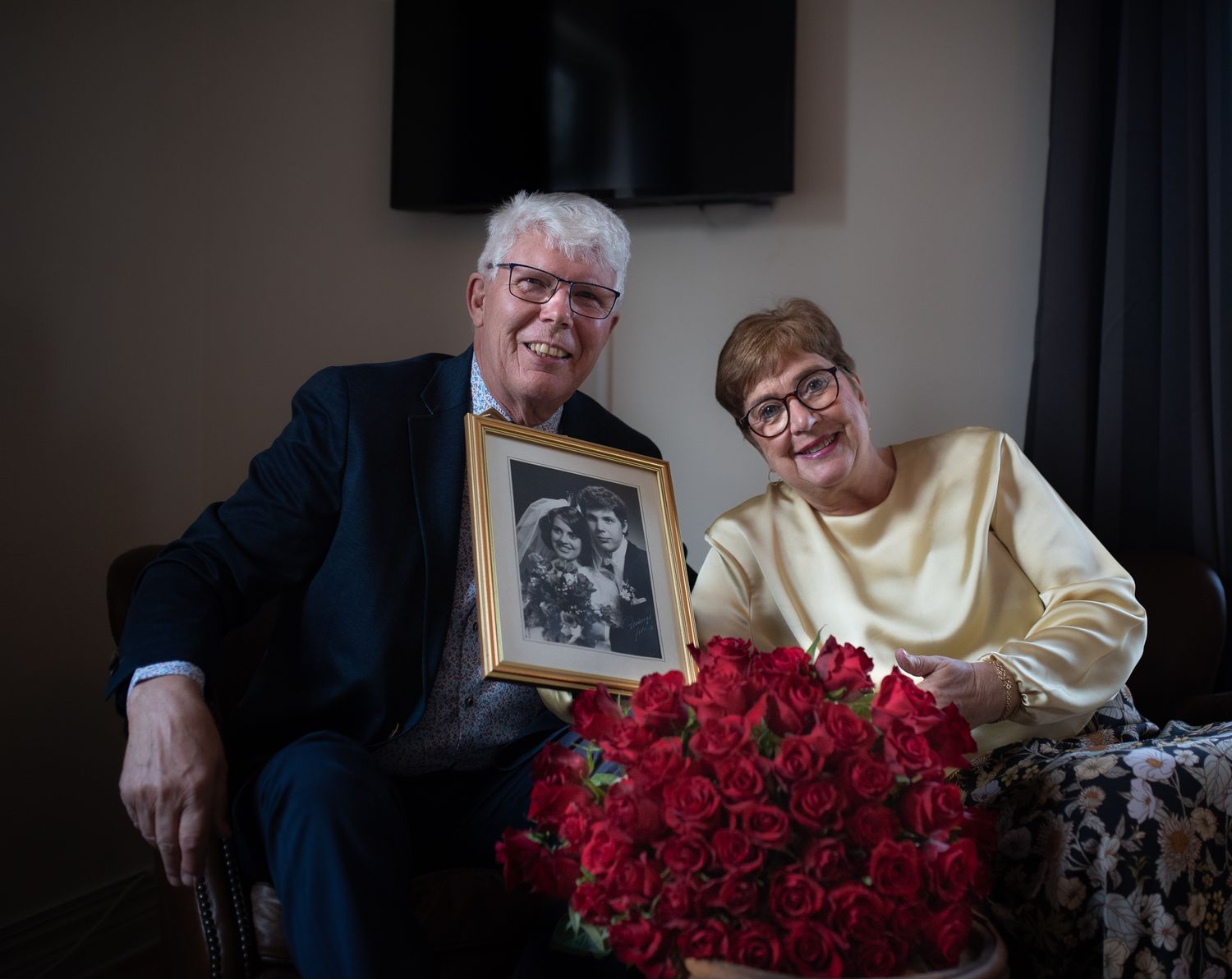 Couple holding vintage photo frame and red roses while sitting in living room.