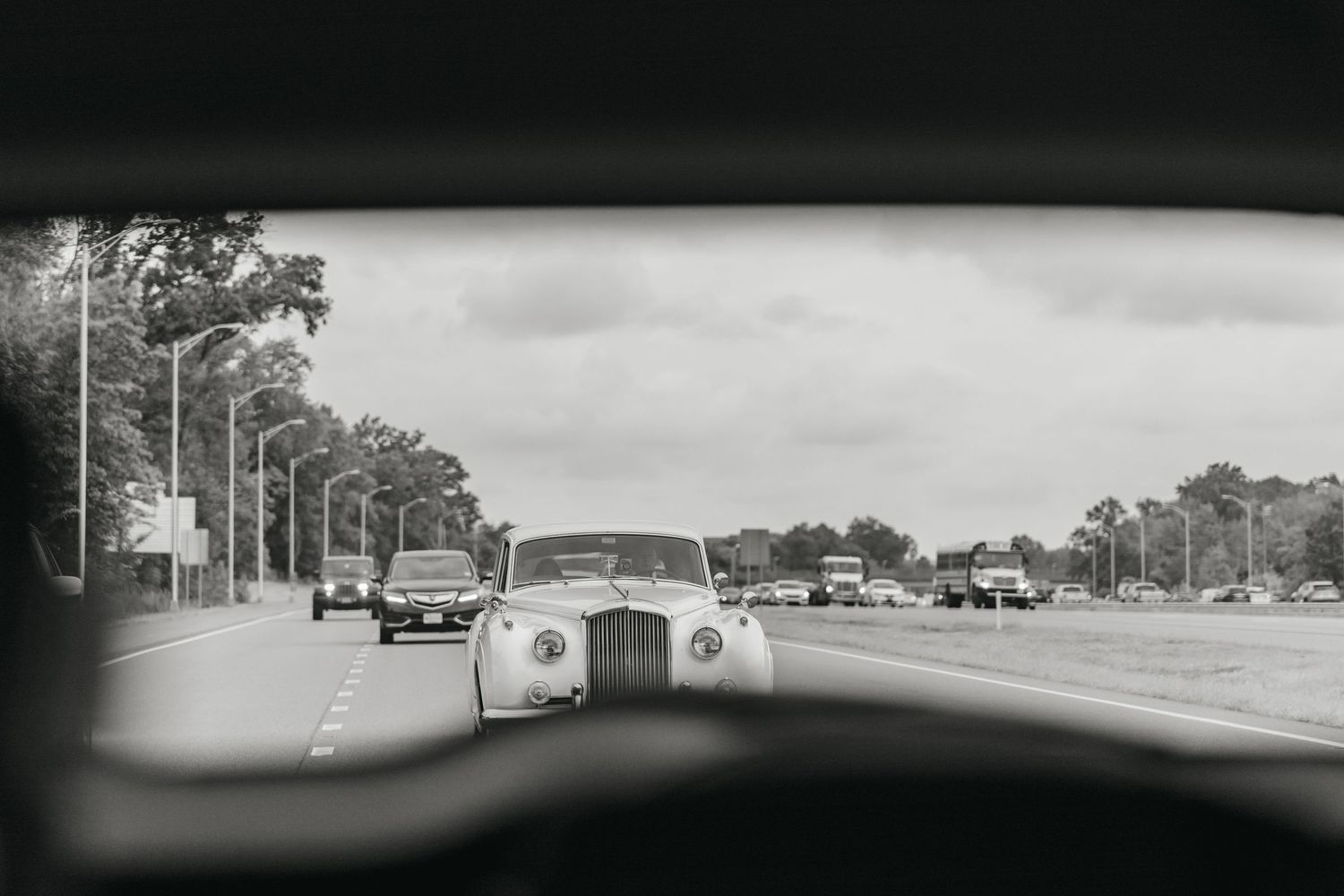 Black and white view of vintage Rolls-Royce wedding car on tree-lined road.