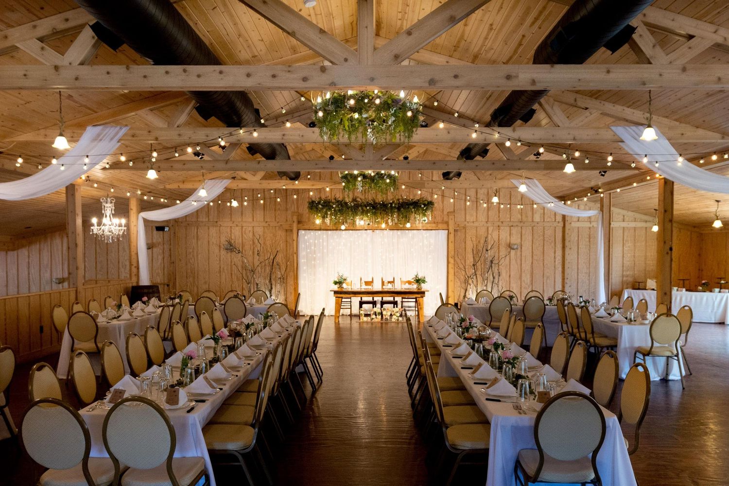 Rustic barn venue with wooden beams and twinkling lights decorated for a wedding reception.