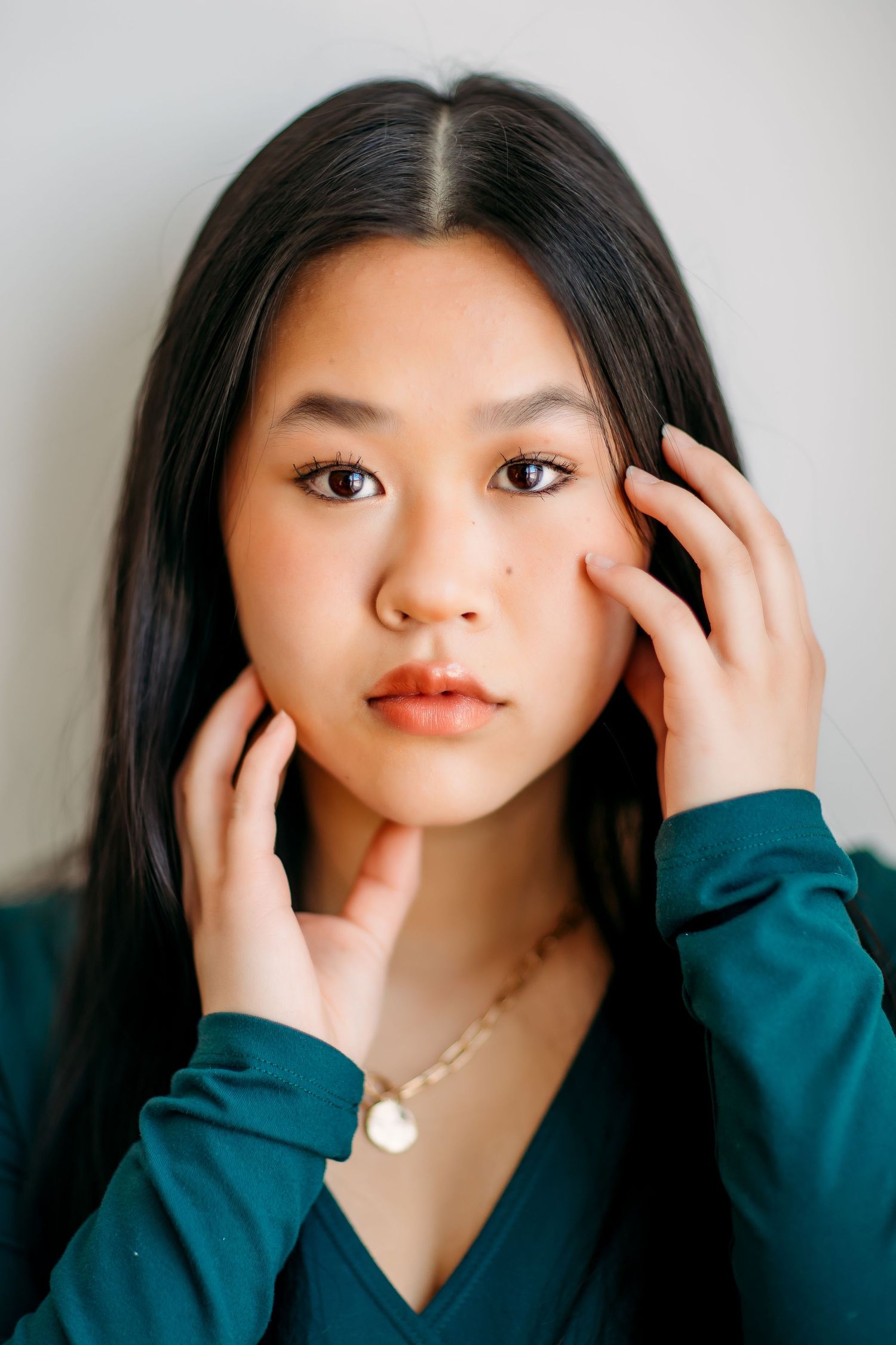 Studio portrait of a young woman in emerald green blouse with delicate gold necklace.