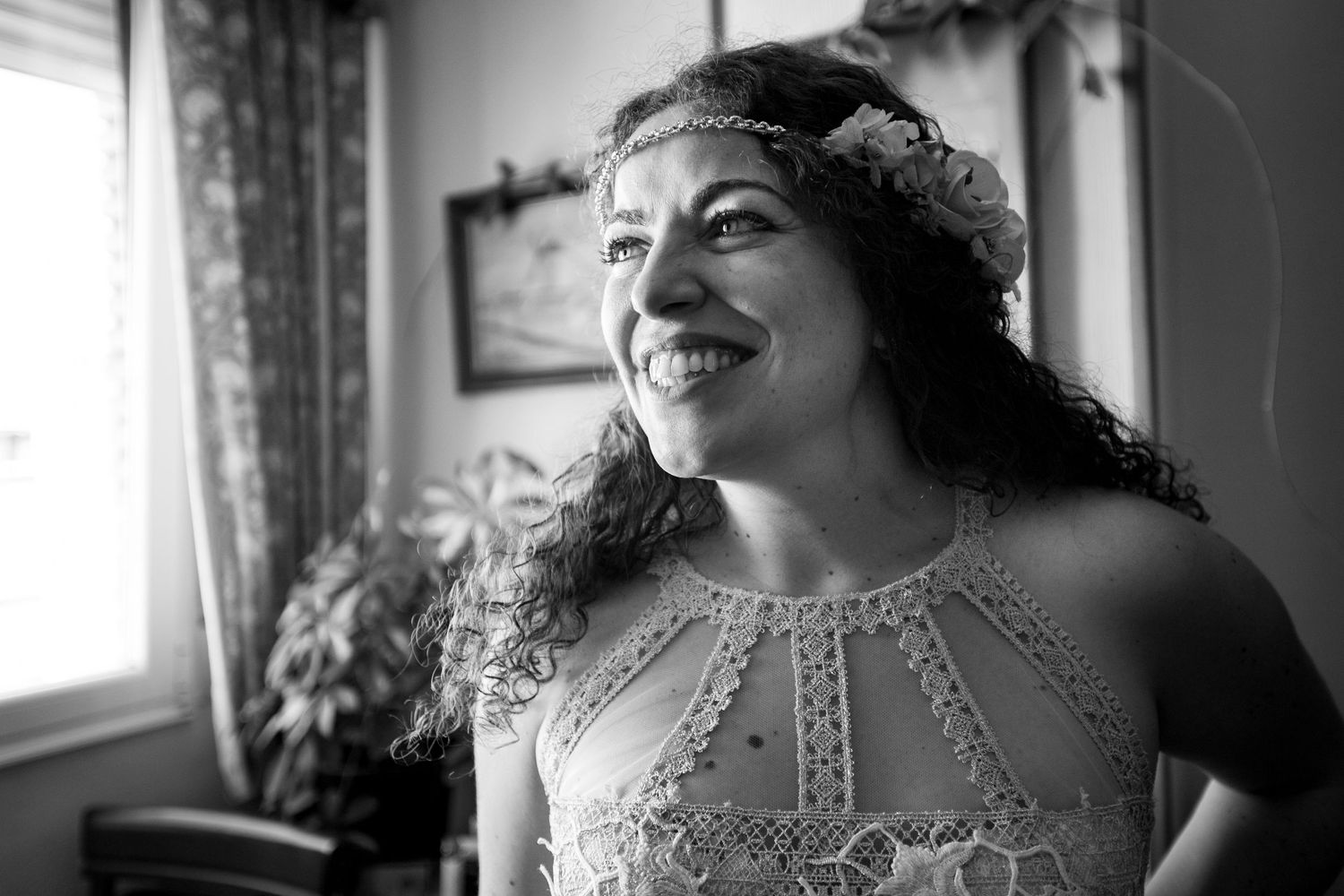 Black and white portrait of a smiling bride in lace dress wearing a floral headpiece indoors.