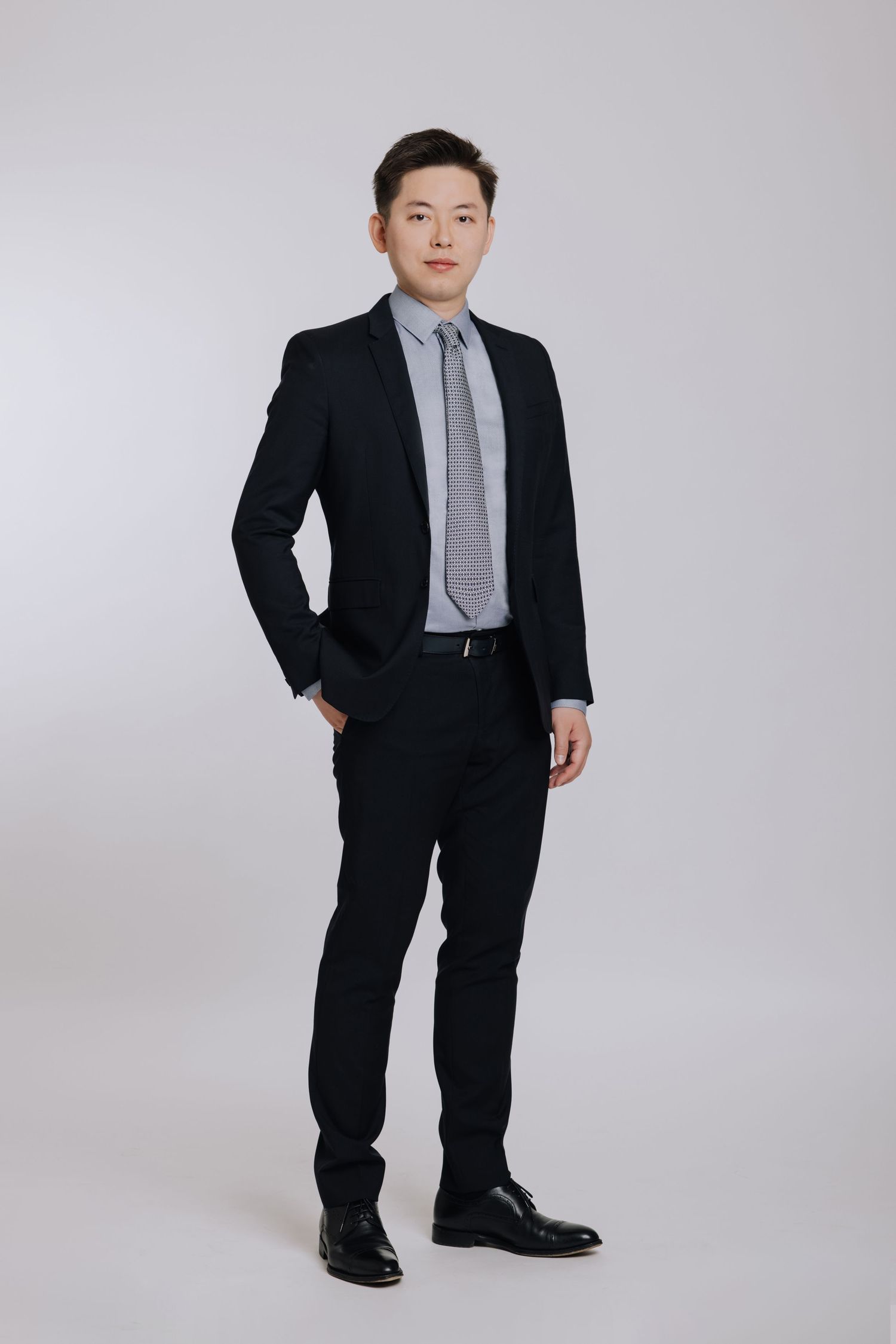 Young Asian businessman in black suit and striped tie posing for a full-length professional portrait.