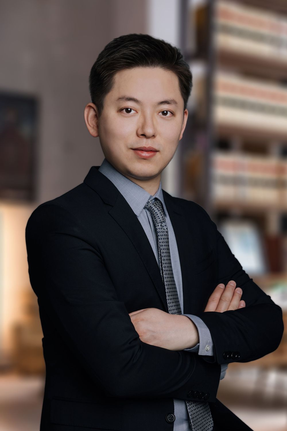 Professional Asian man in black suit with arms crossed posing for a corporate headshot portrait.