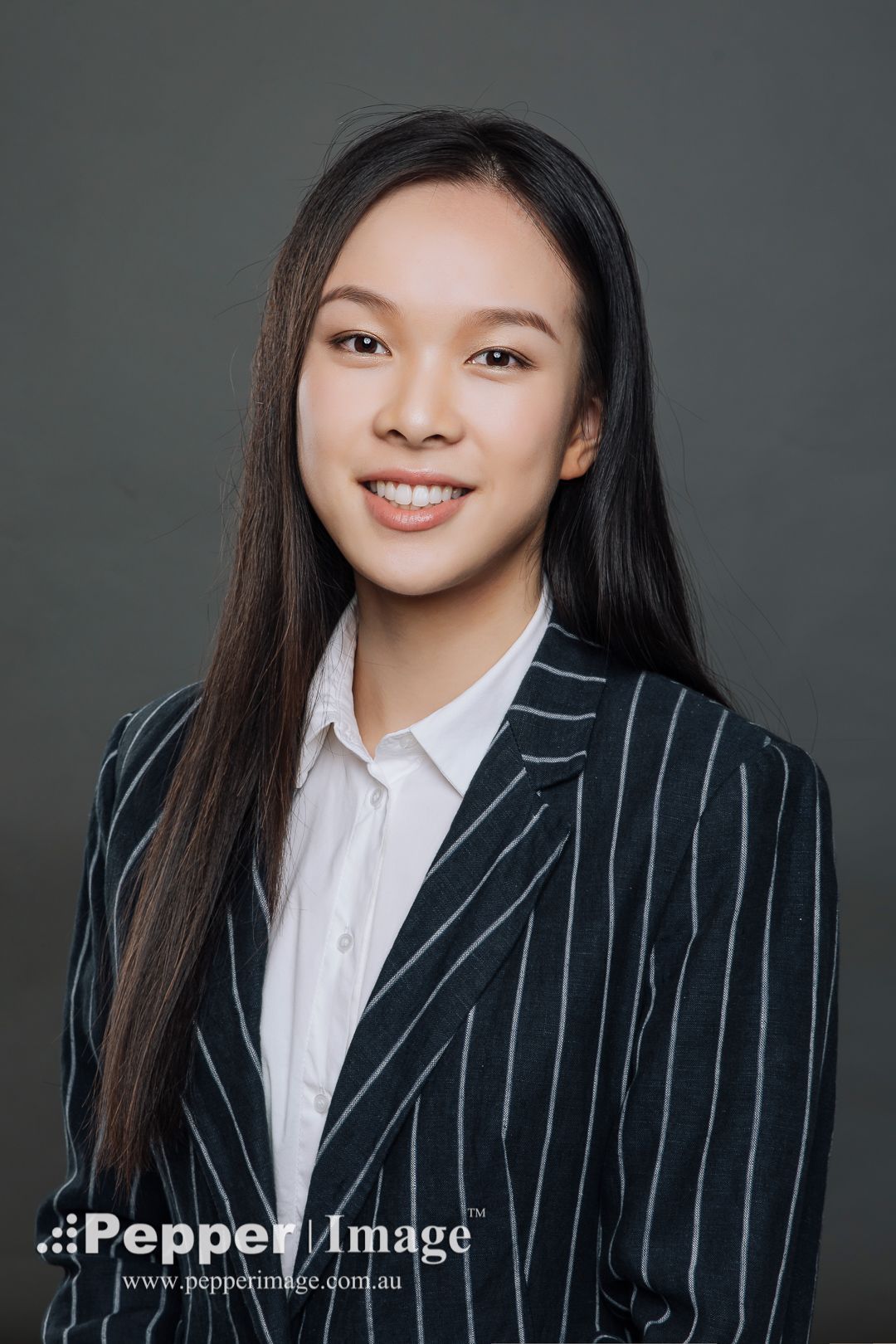 Young woman in striped blazer smiles in a professional corporate headshot portrait.