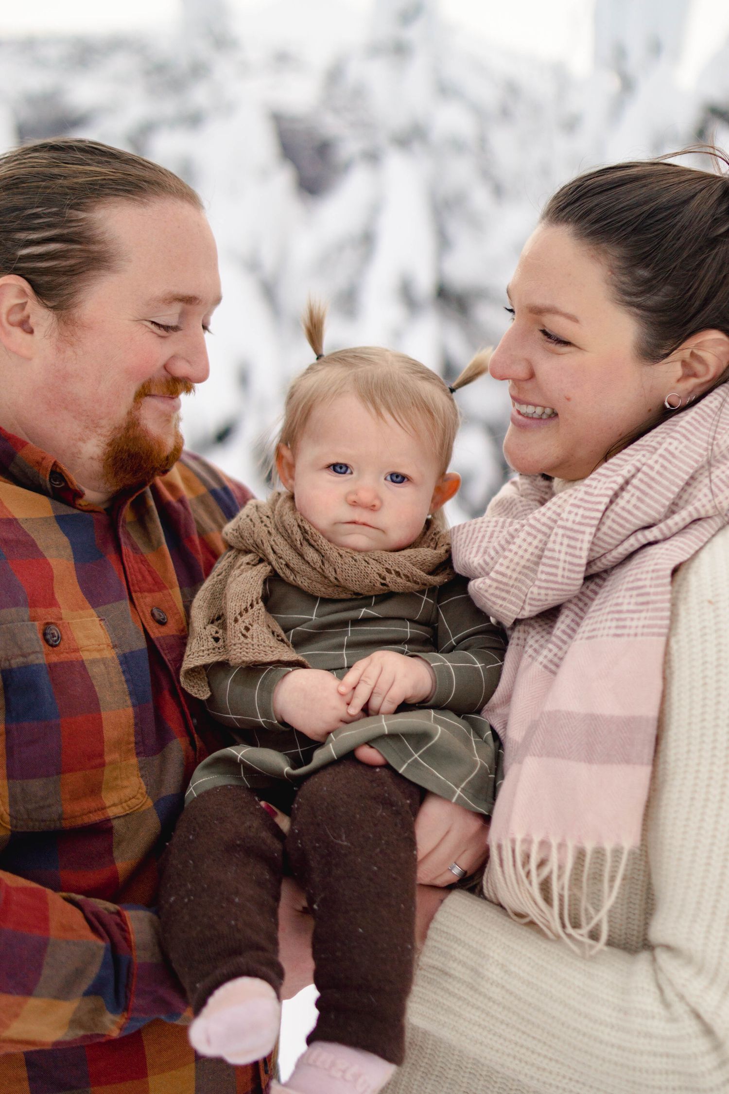 Happy young family with red-bearded father and smiling mother holding cute baby girl in winter snow setting.