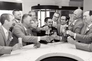 Groom and groomsmen cheers at hotel bar in black and white. Classic and film-inspired wedding photography in Madison, Wisconsin.