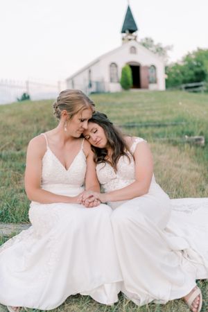 Two brides married sitting on a hill candid in front of a church. Classic and film-inspired wedding photography in Madison, Wisconsin.