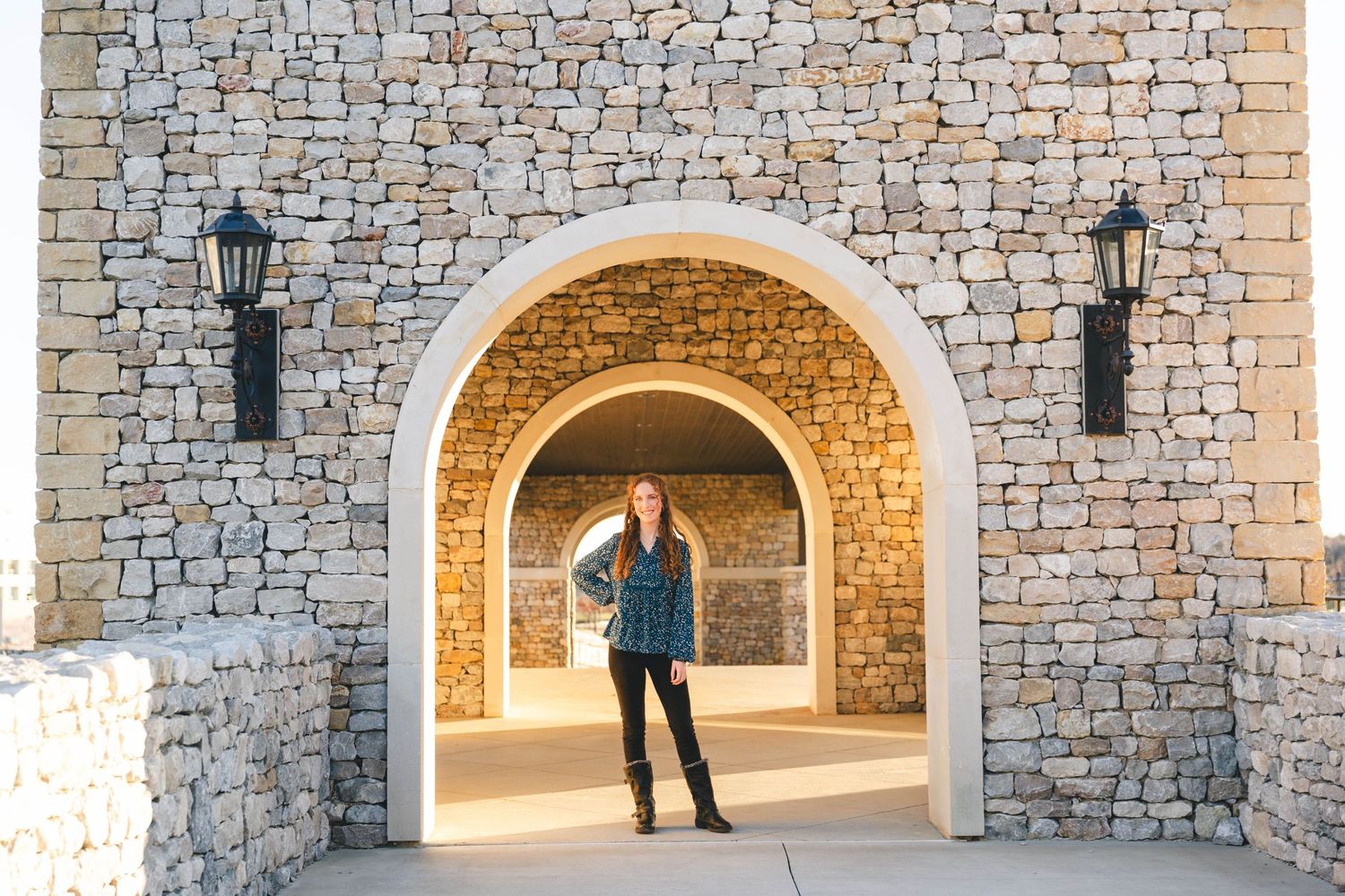 Senior girl stands in stone archway with lanterns during golden hour.