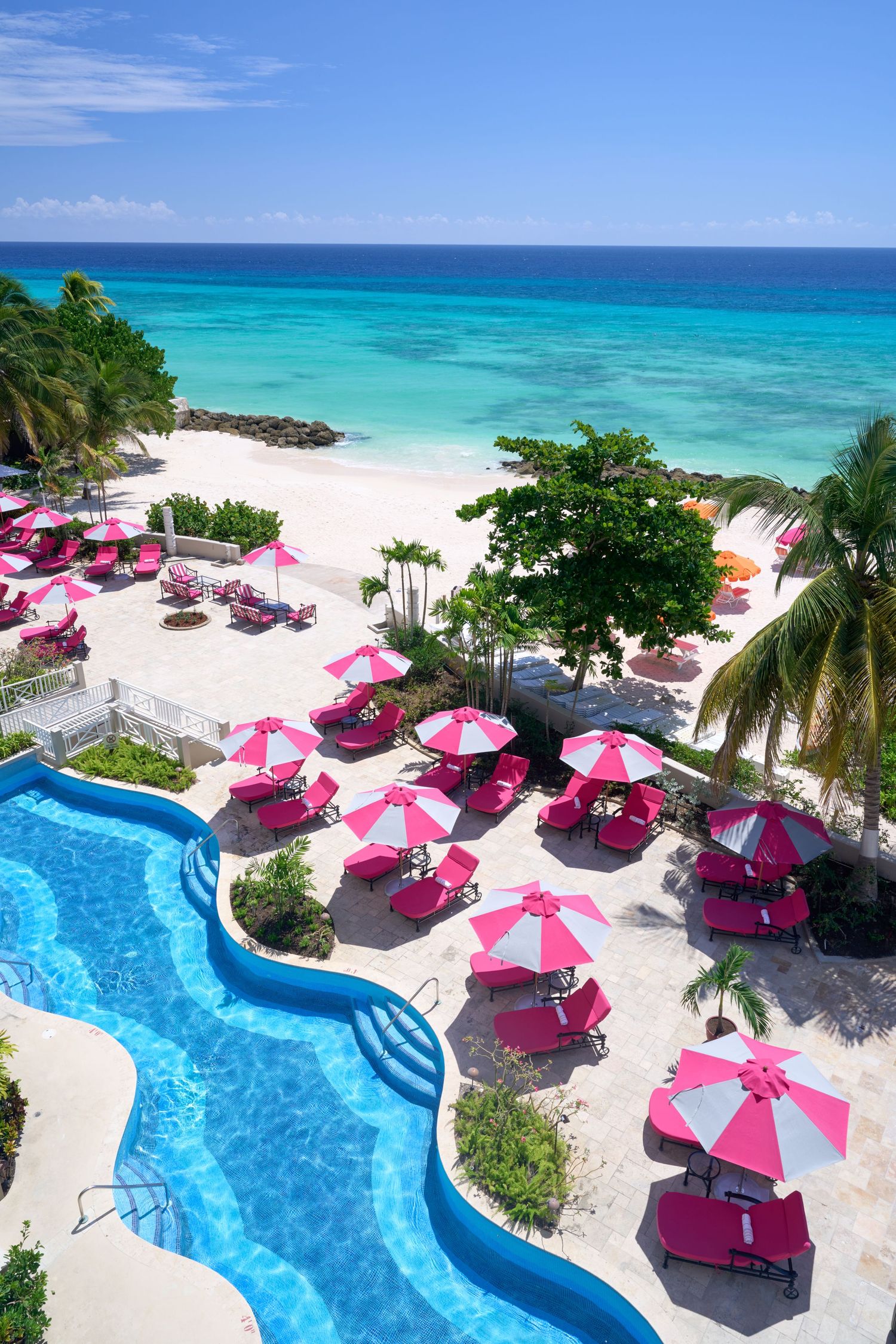 Luxury beachfront resort with curved swimming pool and pink umbrellas overlooking turquoise Caribbean waters.