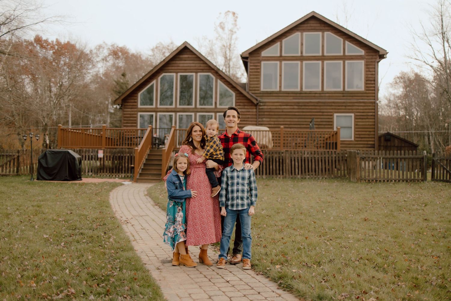 Family group portrait in front of a rustic wooden cabin with large windows.