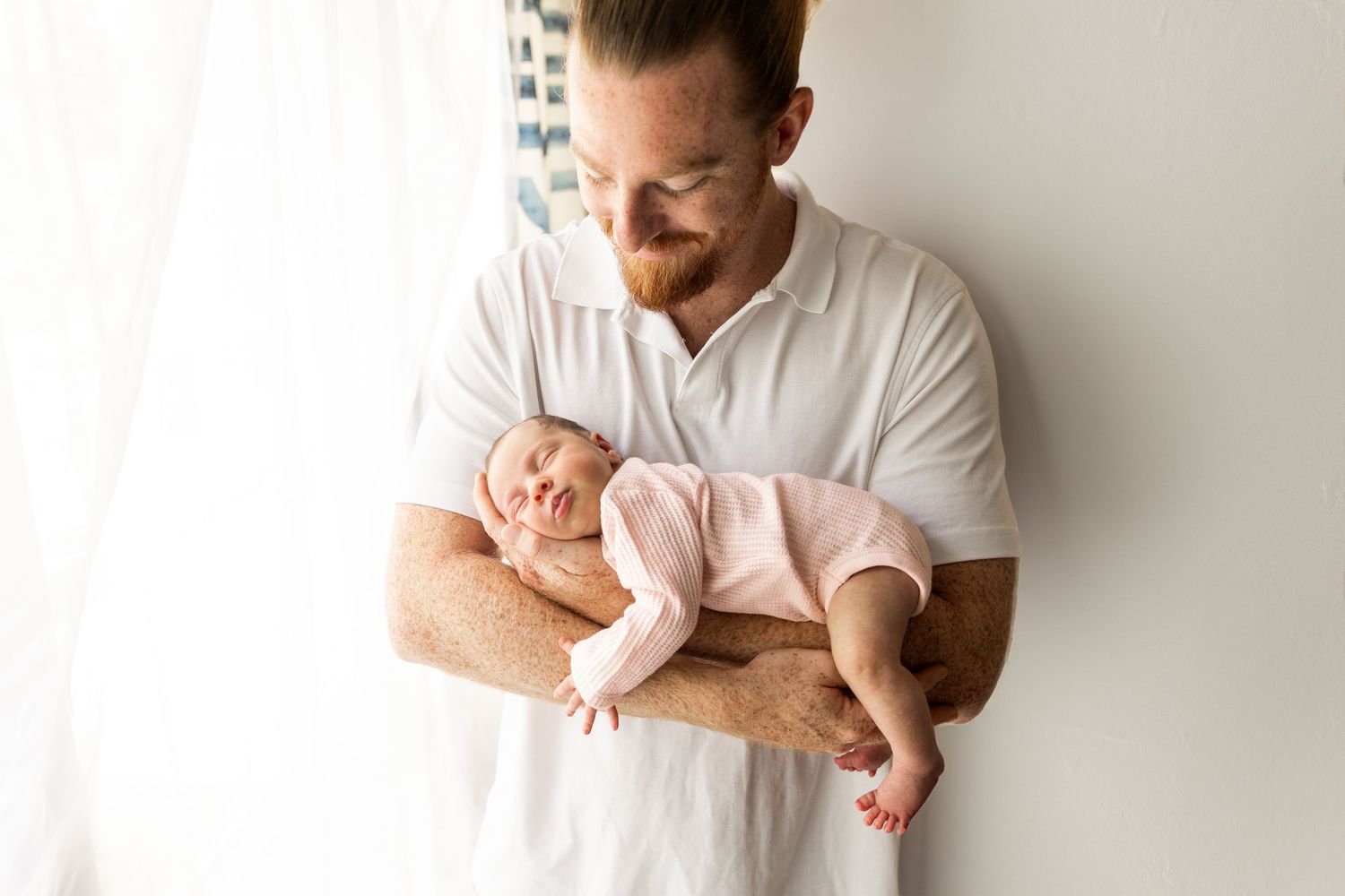 Parent tenderly cradling newborn baby against white wall background.