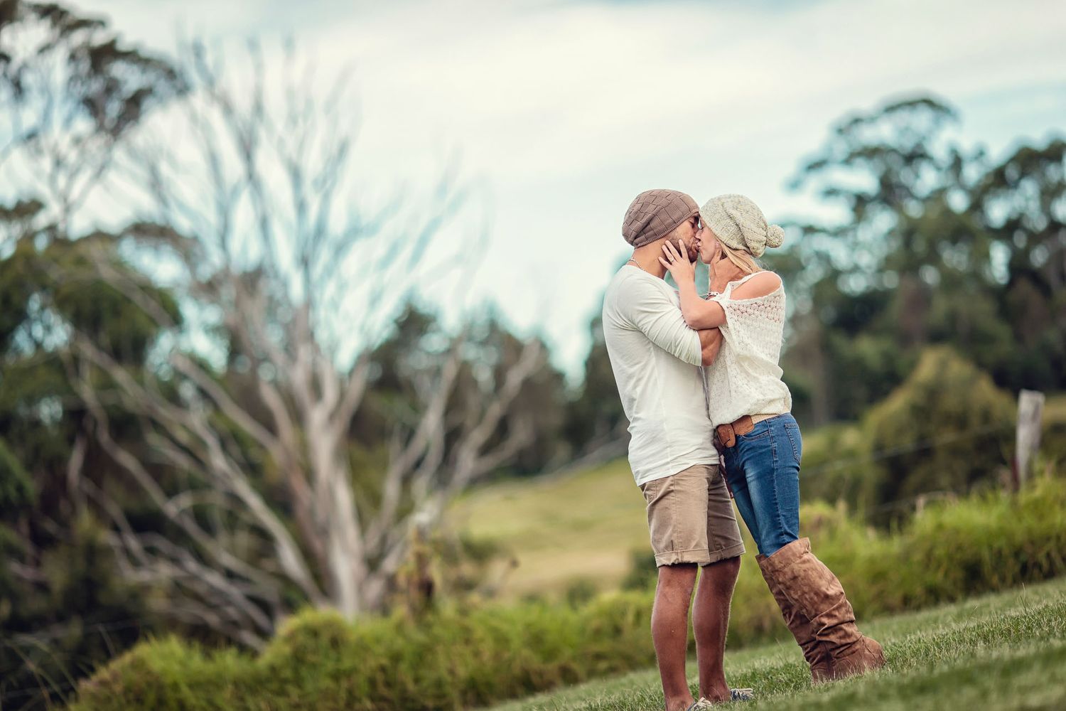 Romantic couple embracing and kissing in a scenic green meadow with trees in background.