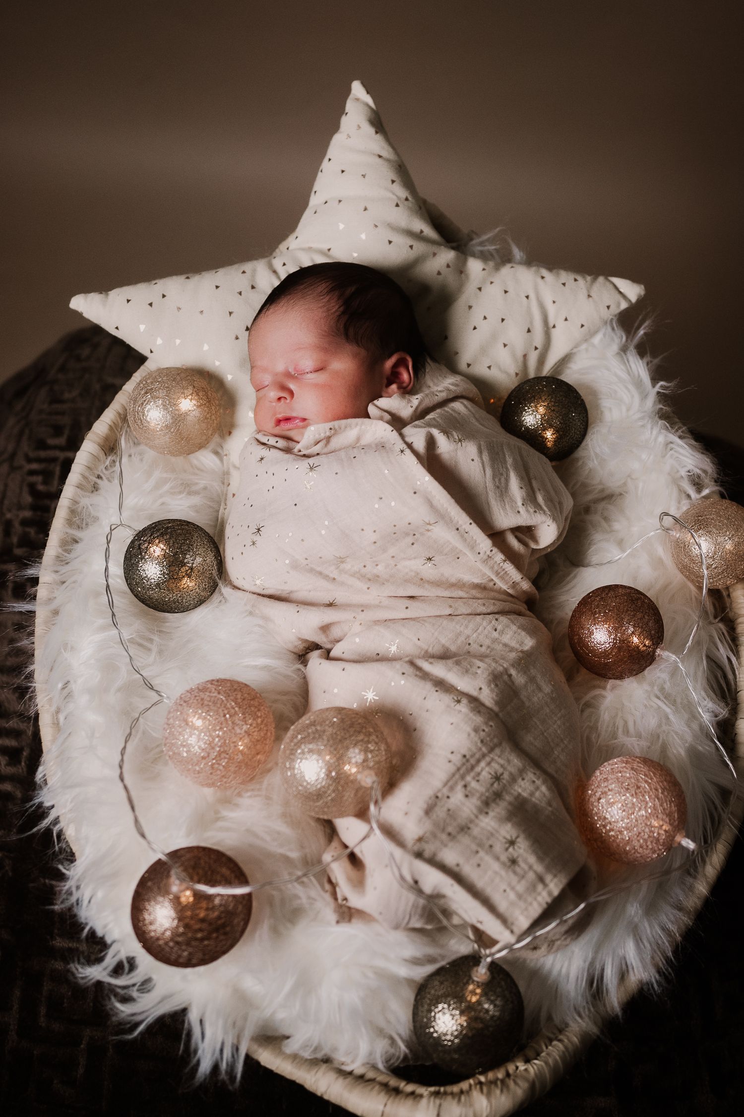 Sleeping newborn baby surrounded by gold Christmas ornaments on a star-shaped pillow.