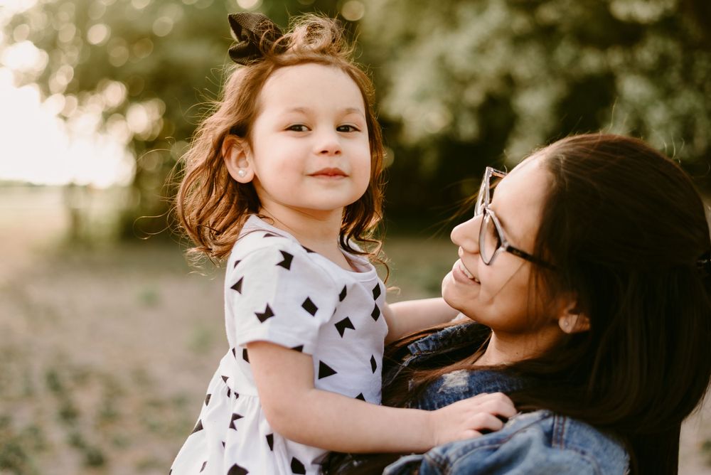 A sweet outdoor moment in nature with a patterned dress and denim jacket under soft lighting.