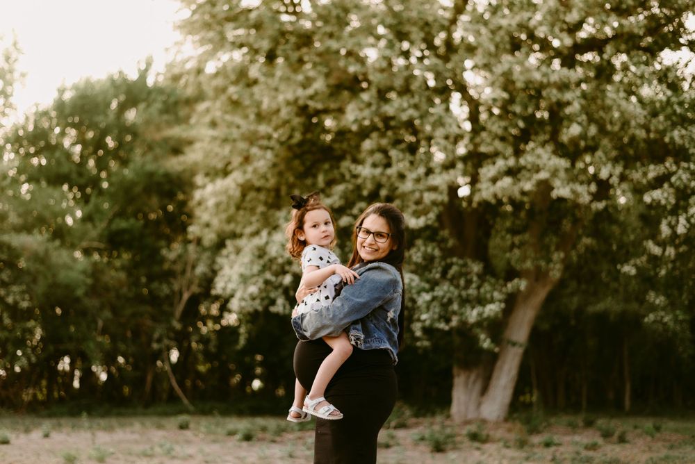 A heartwarming outdoor portrait showing a denim jacket and white patterned dress against blooming trees.