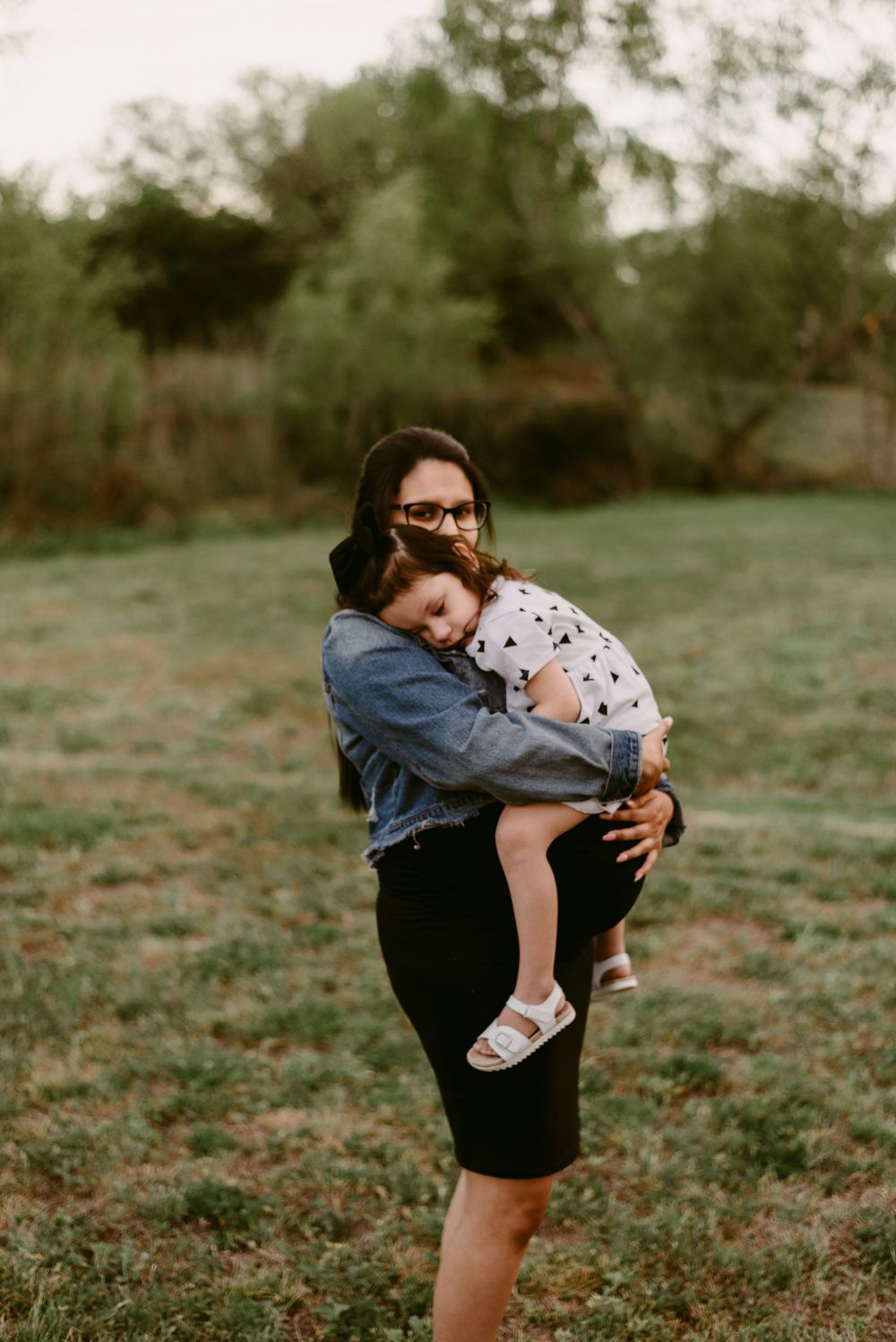 Intimate outdoor portrait with denim jacket and black skirt against green foliage.
