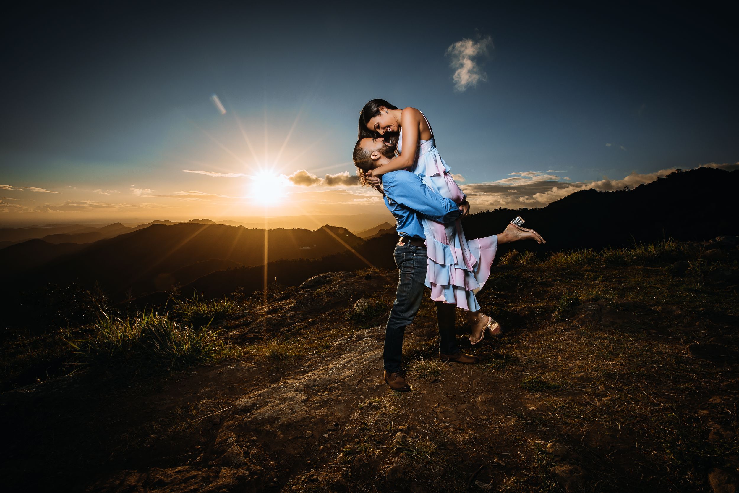 Dramatic sunset engagement photo with couple dancing on mountain peak.