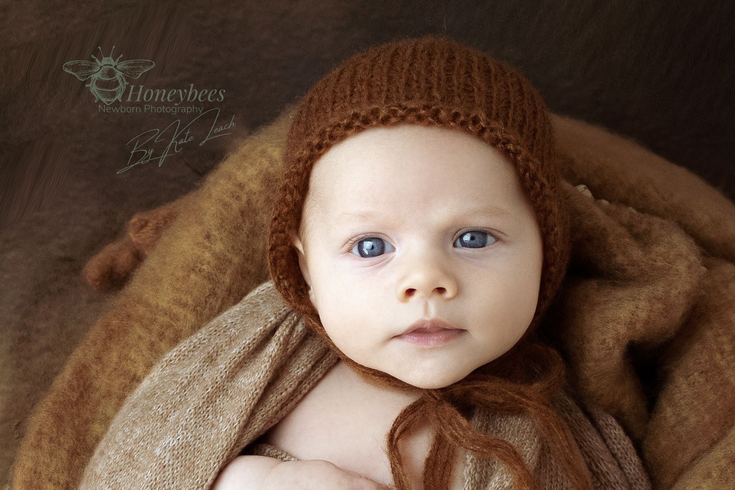 weeks old baby looks at the camera for a photo shoot in brown wraps of natural material knitted Bonet tied under chin