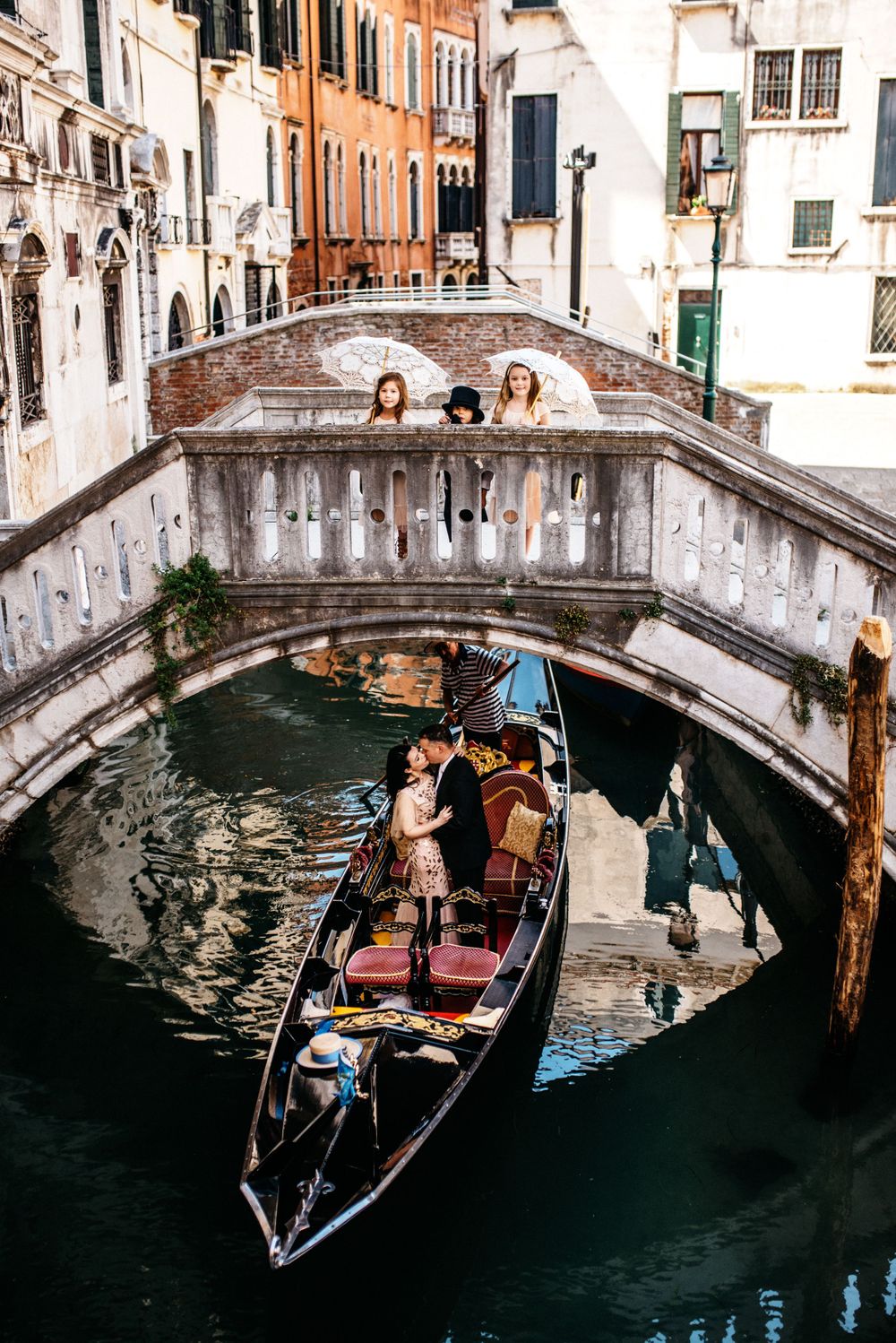 Couple in gondola kissing while kids on over them on the bride in Venice, Italy.