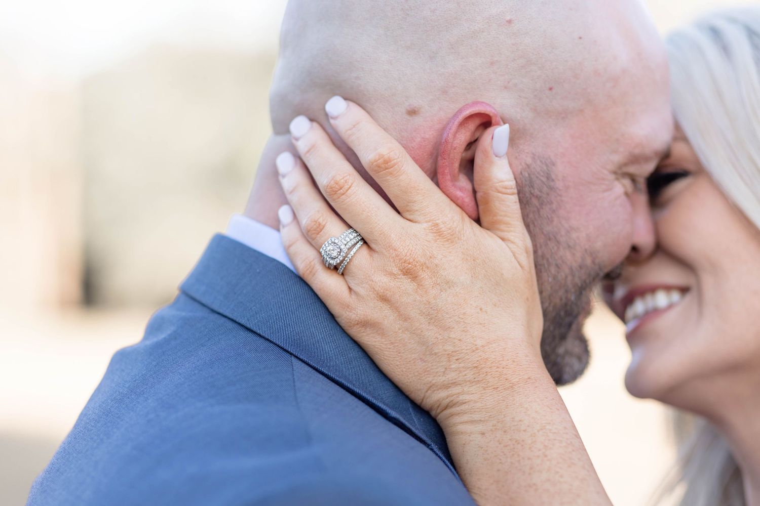 detail of engagement ring while bride and groom kiss