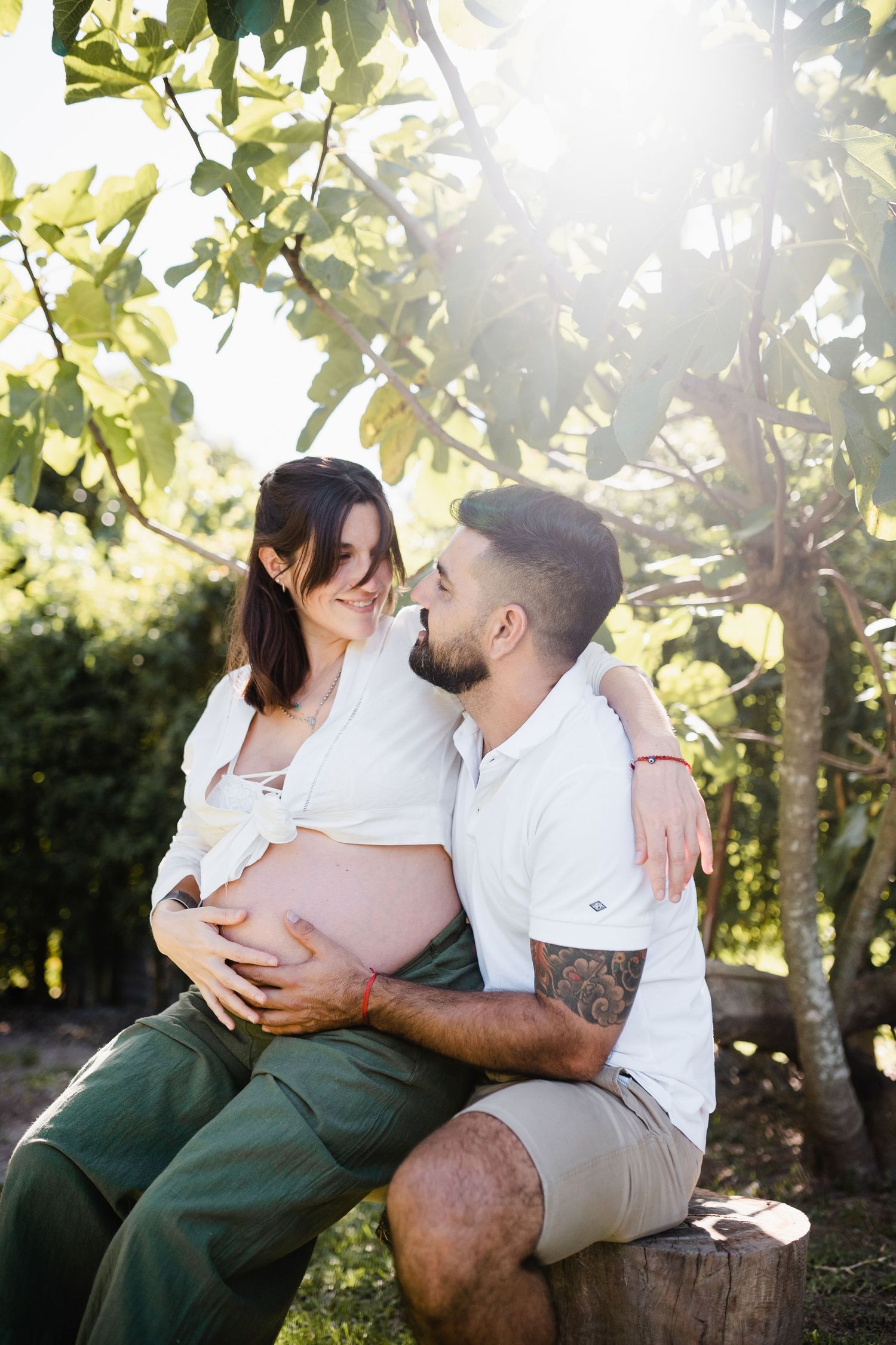 A couple in casual attire sharing tender moments while sitting outdoors in golden sunlight.