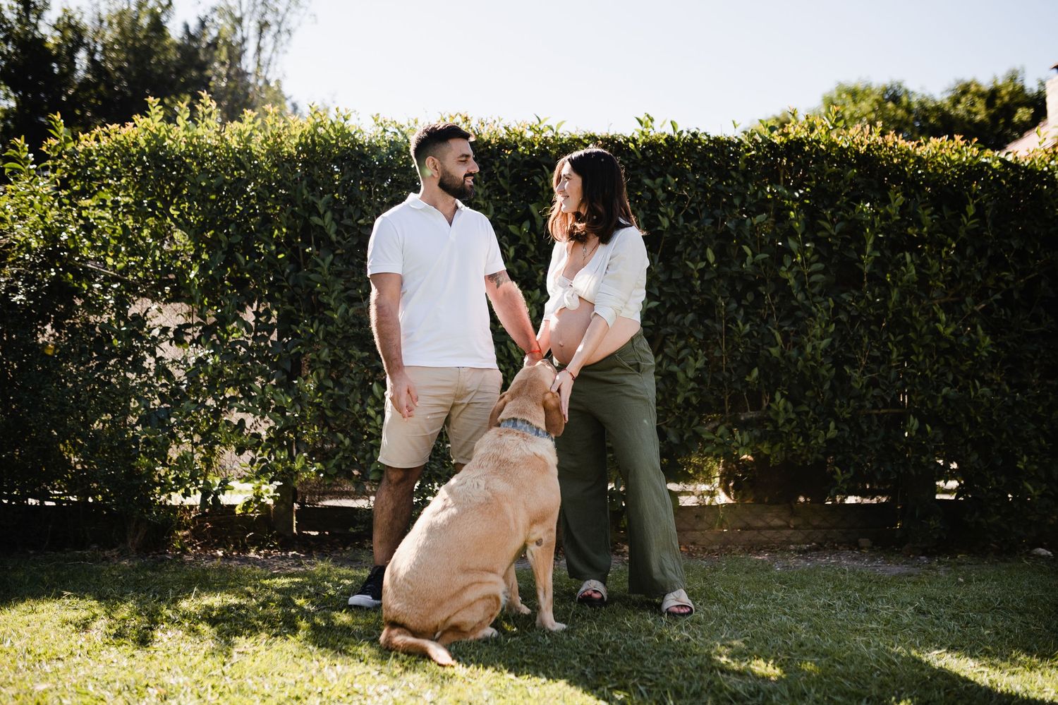 A couple relaxing together on grass with leafy green hedges in the background.