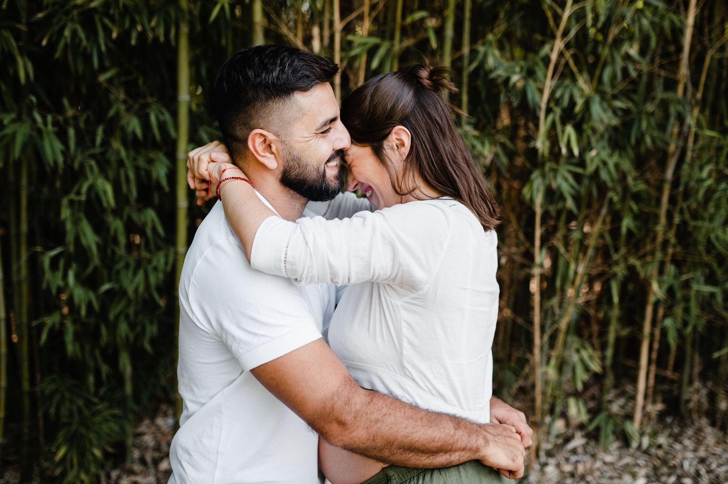 Romantic embrace of couple in white shirts against bamboo background.